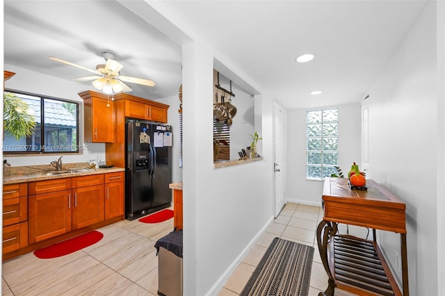 kitchen featuring ceiling fan, sink, light tile patterned floors, light stone counters, and black fridge