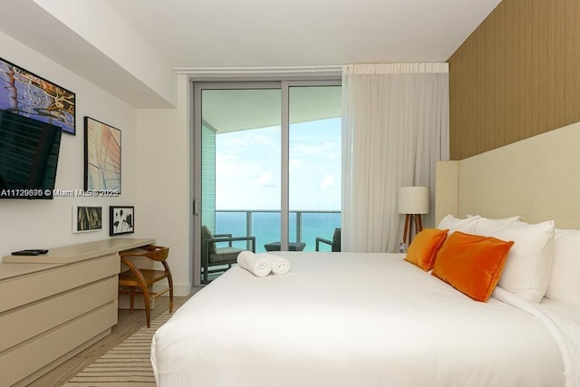 bedroom with light wood-type flooring, access to exterior, a wall of windows, and a water view