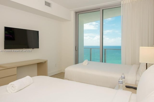 bedroom featuring light wood-type flooring, expansive windows, a water view, and access to outside