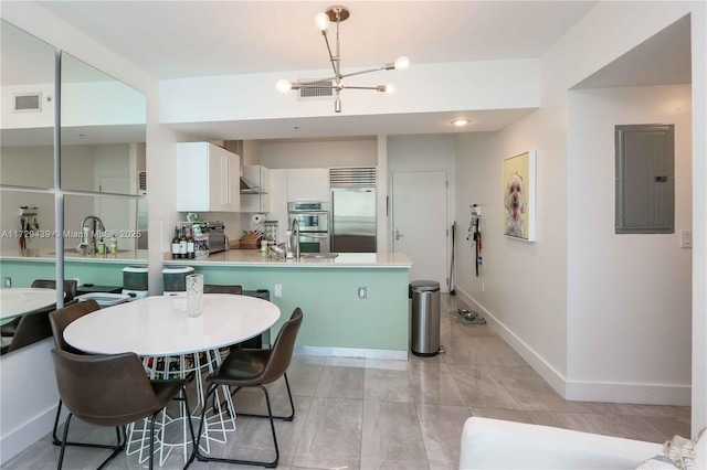 kitchen featuring kitchen peninsula, appliances with stainless steel finishes, electric panel, white cabinetry, and an inviting chandelier