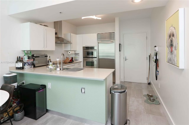 kitchen with kitchen peninsula, sink, wall chimney range hood, and stainless steel appliances