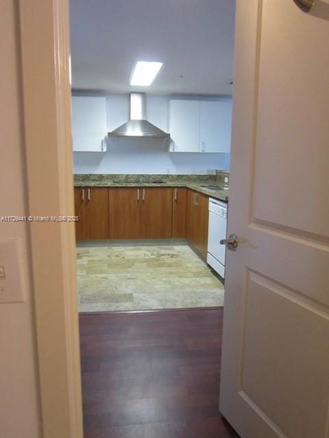 kitchen with wall chimney exhaust hood, white cabinetry, wood-type flooring, sink, and white dishwasher