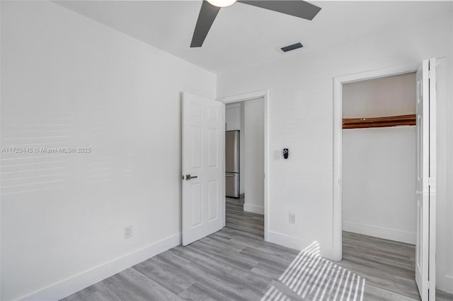 unfurnished bedroom with a spacious closet, ceiling fan, light wood-type flooring, a closet, and stainless steel refrigerator