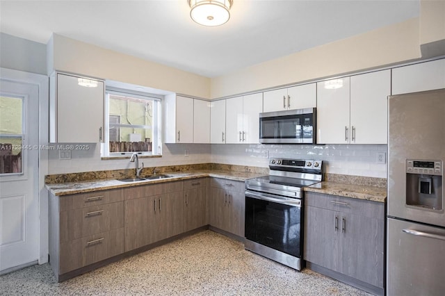 kitchen featuring backsplash, sink, appliances with stainless steel finishes, white cabinets, and stone countertops