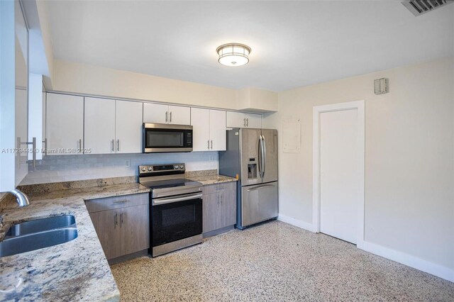 kitchen featuring white cabinetry, appliances with stainless steel finishes, decorative backsplash, light stone counters, and sink