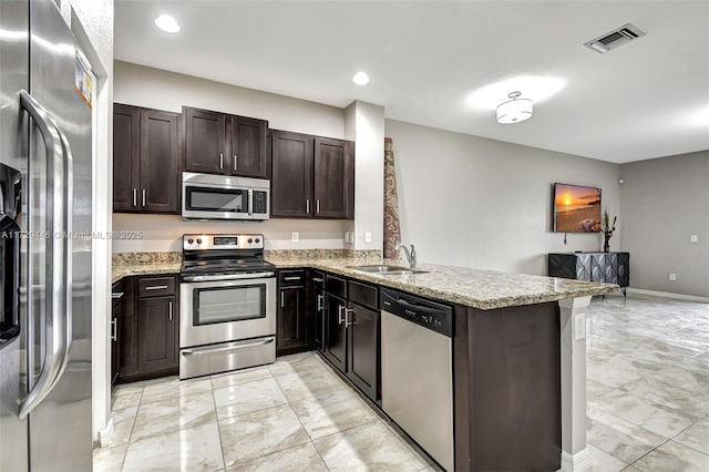 kitchen with appliances with stainless steel finishes, sink, kitchen peninsula, light stone counters, and dark brown cabinets