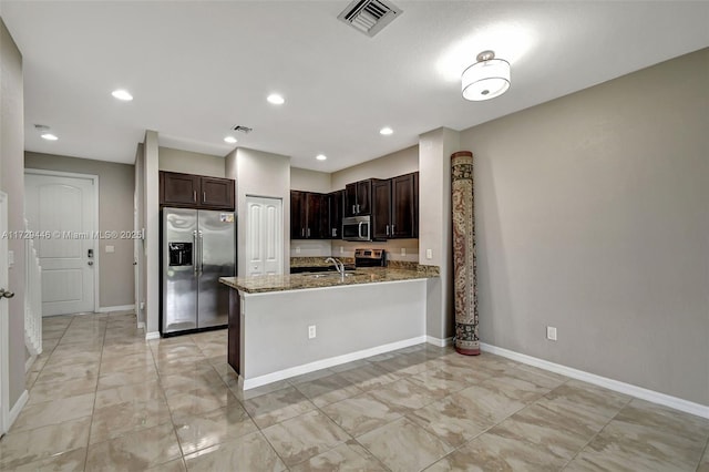 kitchen with kitchen peninsula, stainless steel appliances, dark brown cabinets, light stone counters, and sink