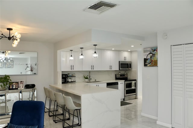 kitchen with kitchen peninsula, hanging light fixtures, a kitchen breakfast bar, stainless steel appliances, and white cabinets