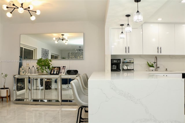 kitchen with light stone countertops, white cabinets, decorative light fixtures, sink, and a chandelier