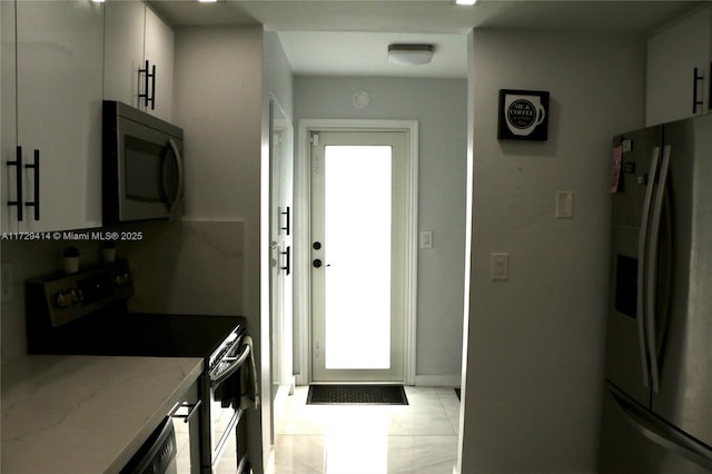 kitchen with light stone countertops, white cabinetry, light tile patterned floors, and stainless steel appliances