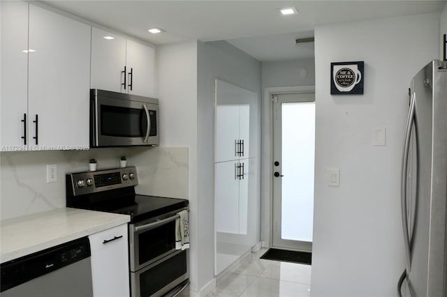 kitchen with light stone countertops, white cabinets, stainless steel appliances, backsplash, and light tile patterned flooring