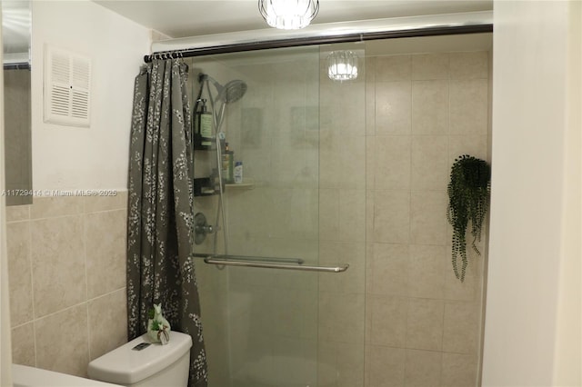 bathroom featuring toilet, tile walls, and a shower with door