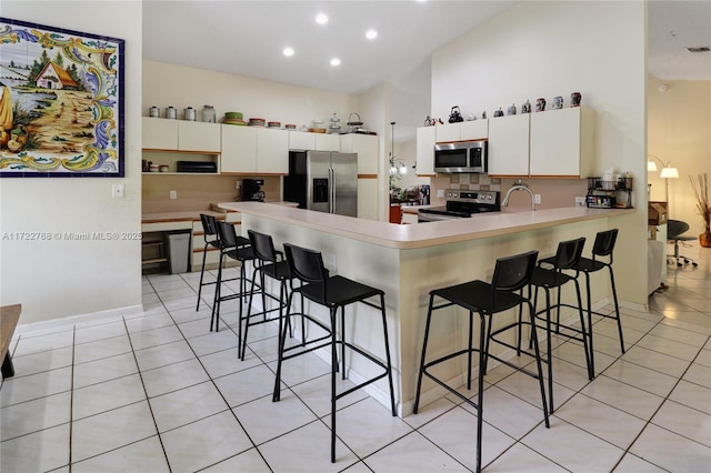 kitchen featuring light tile patterned floors, kitchen peninsula, appliances with stainless steel finishes, and a kitchen breakfast bar