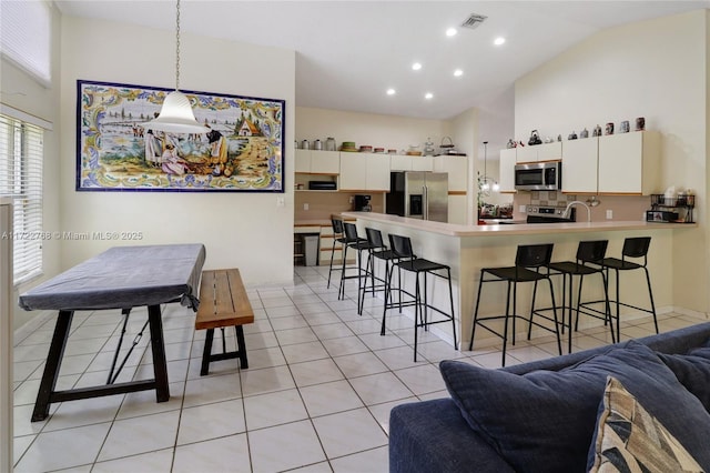 kitchen featuring a breakfast bar, stainless steel appliances, white cabinetry, and hanging light fixtures