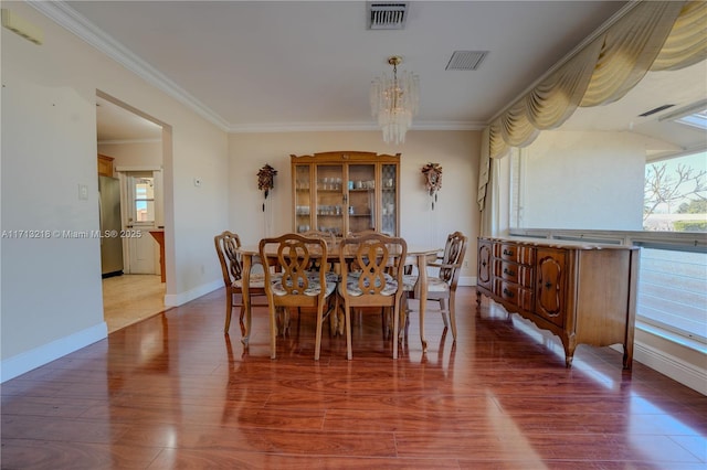 dining area with a healthy amount of sunlight, an inviting chandelier, ornamental molding, and hardwood / wood-style flooring