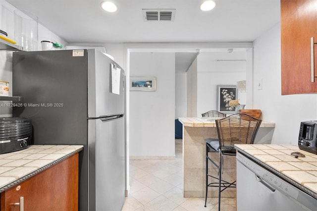 300 Bayview Dr Unit 1503, Sunny Isles Beach, FL 33160 - kitchen featuring stainless steel appliances, tile counters, brown cabinetry, recessed lighting, and light tile patterned floors