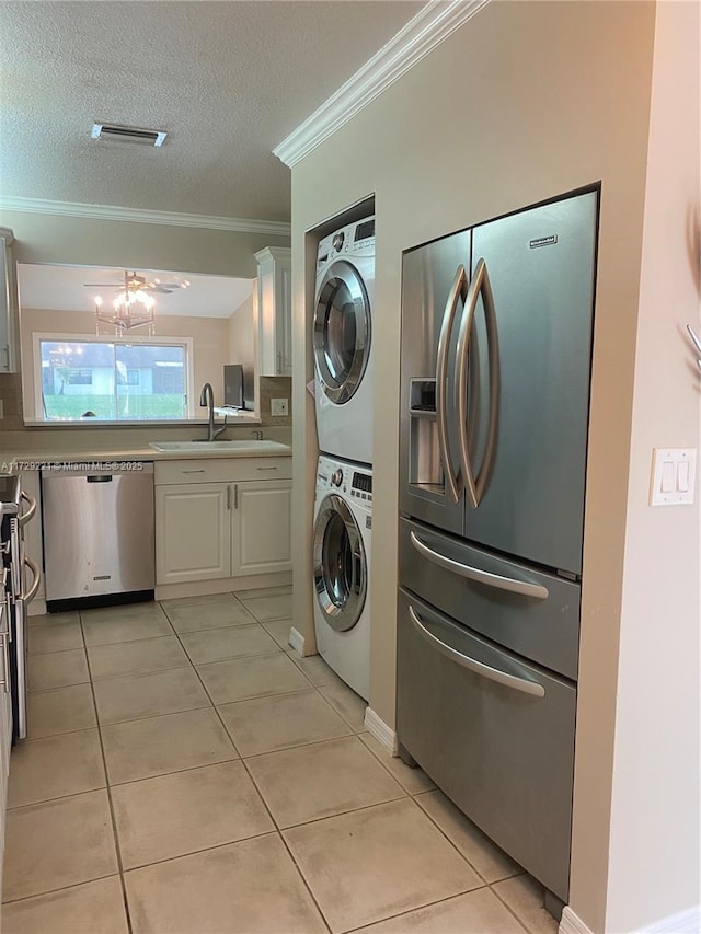 laundry area with sink, a textured ceiling, light tile patterned floors, and stacked washer and dryer