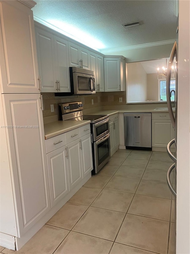 kitchen with appliances with stainless steel finishes, white cabinets, ornamental molding, light tile patterned floors, and a textured ceiling