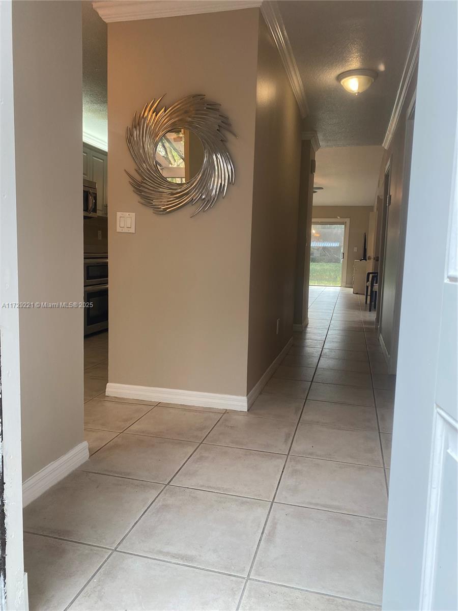 hall featuring a textured ceiling, light tile patterned floors, and ornamental molding