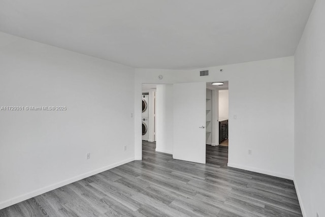 empty room with wood-type flooring and stacked washer / dryer