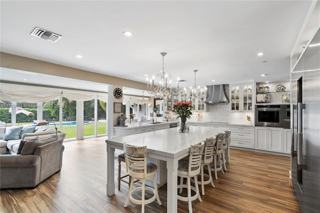 kitchen with wall chimney range hood, sink, stainless steel appliances, a spacious island, and white cabinets