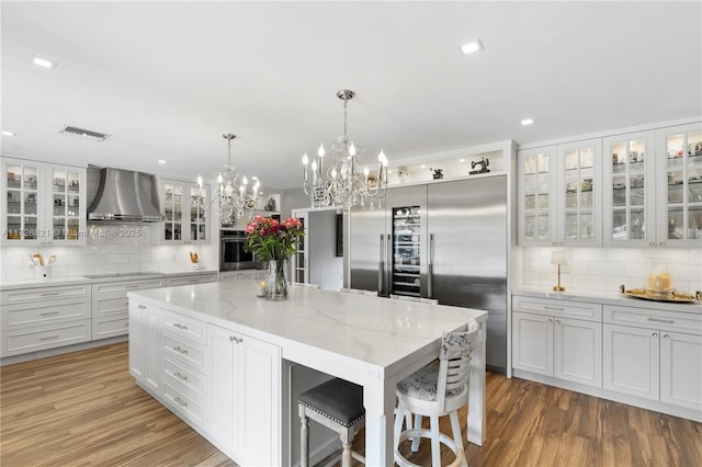 kitchen with wall chimney exhaust hood, a breakfast bar area, a kitchen island, stainless steel appliances, and light stone countertops