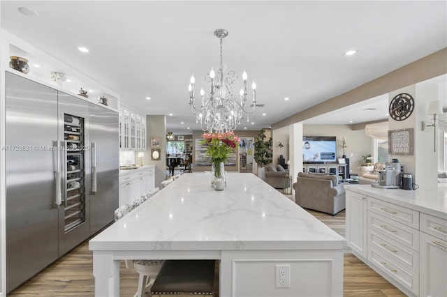 kitchen with white cabinetry, a center island, stainless steel built in fridge, and light stone counters