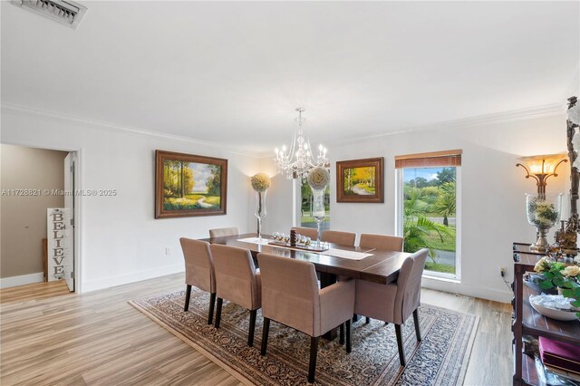 dining space featuring crown molding, an inviting chandelier, and light hardwood / wood-style flooring