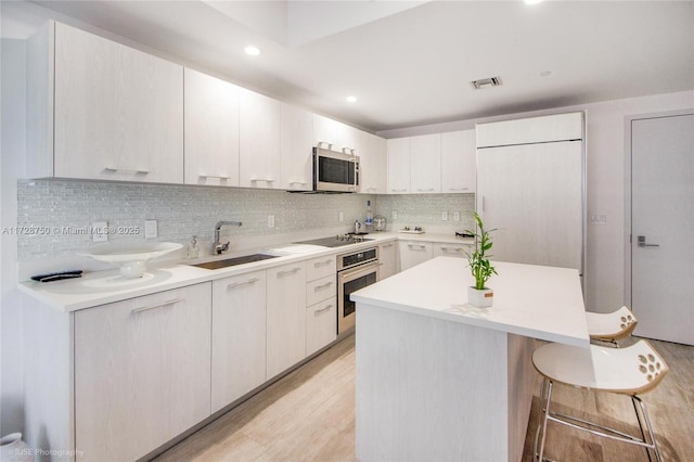 kitchen featuring white cabinetry, a kitchen bar, stainless steel appliances, light hardwood / wood-style flooring, and sink