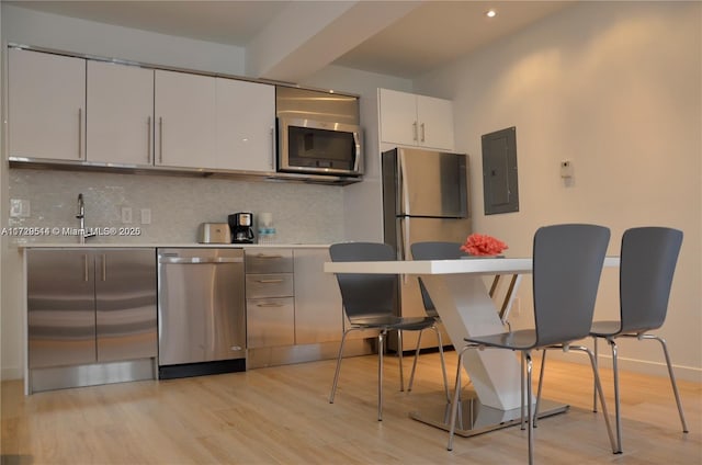 kitchen with appliances with stainless steel finishes, white cabinetry, tasteful backsplash, light wood-type flooring, and electric panel