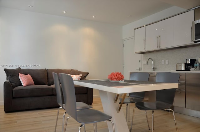 kitchen featuring white cabinets, decorative backsplash, sink, a breakfast bar, and light hardwood / wood-style flooring