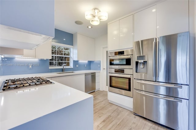 kitchen featuring sink, appliances with stainless steel finishes, an inviting chandelier, light hardwood / wood-style floors, and white cabinets