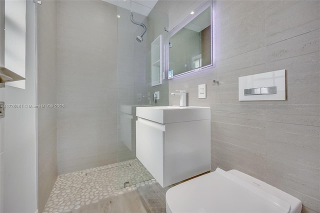 bathroom with vanity, a tile shower, tile walls, and toilet