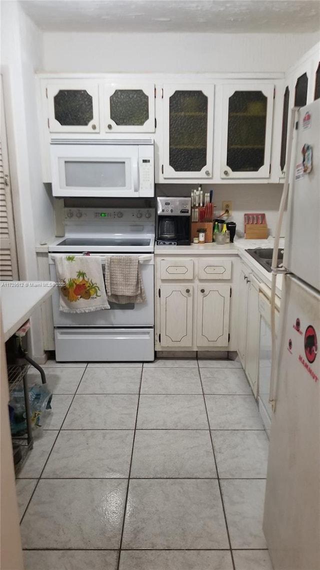 kitchen with white appliances, sink, light tile patterned floors, and white cabinets