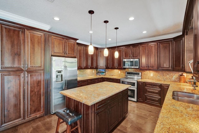 kitchen with a kitchen island, stainless steel appliances, hanging light fixtures, light stone counters, and crown molding