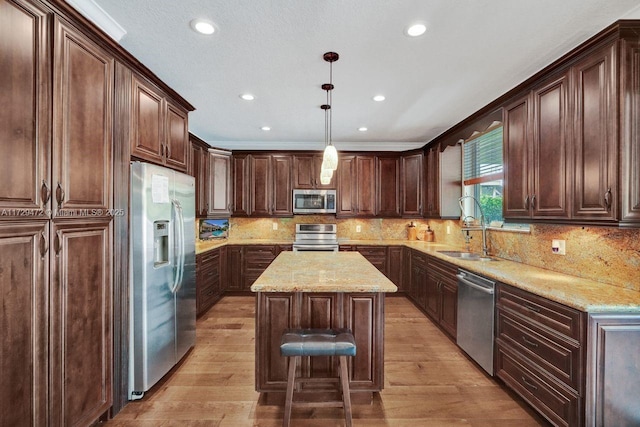 kitchen featuring a kitchen island, decorative light fixtures, stainless steel appliances, sink, and crown molding