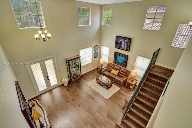 living room featuring a towering ceiling, a chandelier, hardwood / wood-style floors, and french doors