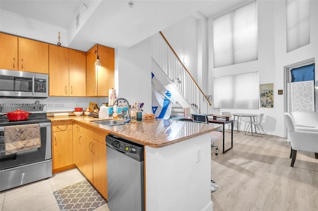 kitchen with kitchen peninsula, appliances with stainless steel finishes, a high ceiling, light stone counters, and sink