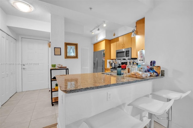 kitchen with light tile patterned floors, kitchen peninsula, appliances with stainless steel finishes, stone countertops, and sink