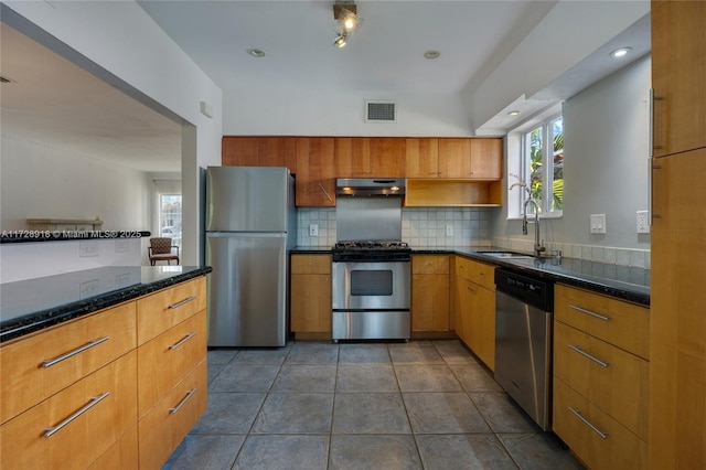 kitchen with sink, tasteful backsplash, appliances with stainless steel finishes, dark tile patterned flooring, and dark stone counters