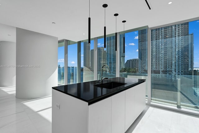 kitchen with white cabinets, sink, hanging light fixtures, a kitchen island with sink, and floor to ceiling windows