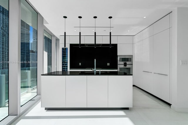 kitchen featuring pendant lighting, white cabinetry, an island with sink, sink, and expansive windows