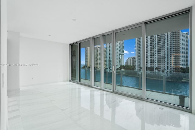 unfurnished room featuring a wall of windows, a water view, and a city view