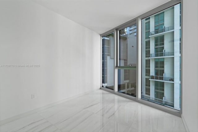 spare room featuring baseboards, marble finish floor, and floor to ceiling windows