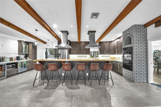 kitchen featuring appliances with stainless steel finishes, a kitchen island with sink, island range hood, dark brown cabinets, and wine cooler