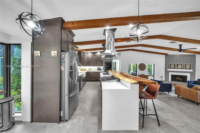 kitchen with dark brown cabinets, stainless steel fridge with ice dispenser, a brick fireplace, vaulted ceiling with beams, and island range hood