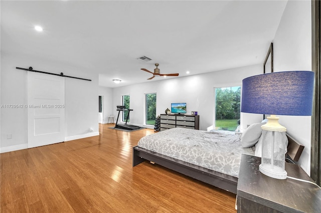 bedroom featuring hardwood / wood-style flooring, ceiling fan, and a barn door