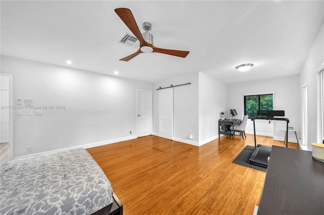 workout area with hardwood / wood-style flooring, ceiling fan, and a barn door