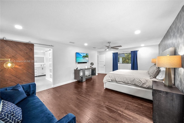 bedroom with connected bathroom, ceiling fan, a barn door, and dark hardwood / wood-style flooring