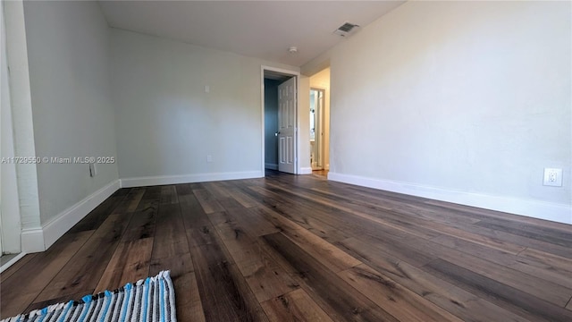 empty room featuring visible vents, baseboards, and dark wood-type flooring